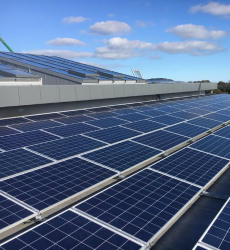 Commercial rooftop solar panels installed on a modern building, harnessing renewable energy under a clear blue sky. ARC Renewables provides expert solar solutions for businesses across the UK.